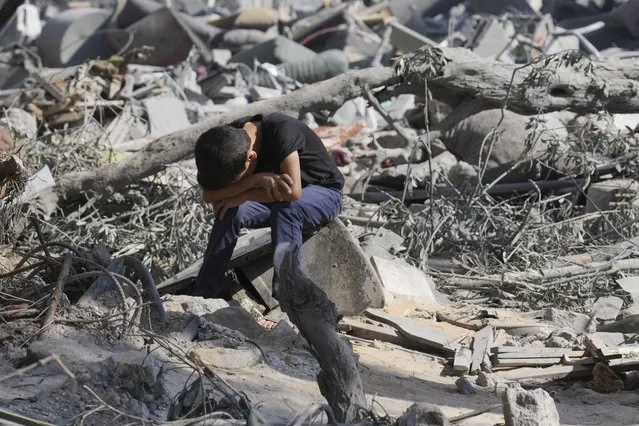 A Palestinian boy sits on the rubble of the building destroyed in an Israeli airstrike in Bureij refugee camp Gaza Strip, Wednesday, October 18, 2023. (Photo by Hatem Moussa/AP Photo)