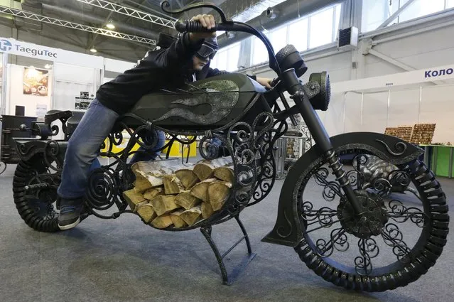 A boy poses for a picture while sitting on an iron forged barbecue, also known as “mangal”, which depicts a motorcycle and was made by owner of a private smithy Dmitry Fanin (not pictured), during an annual welding and metalwork exhibition in Krasnoyarsk, Russia, February 2, 2016. (Photo by Ilya Naymushin/Reuters)