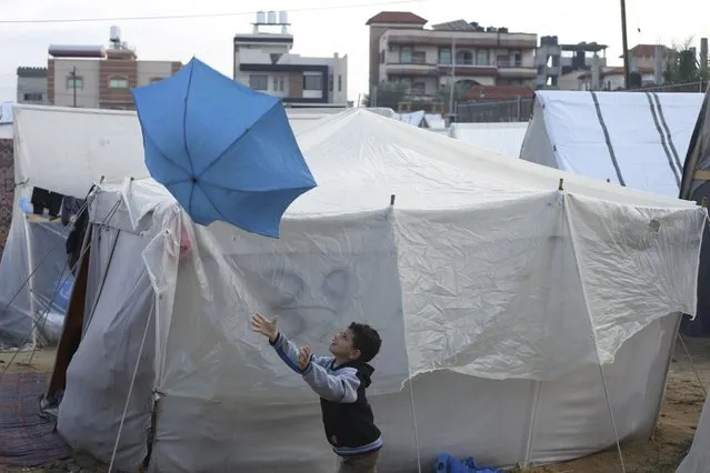 A Palestinian boy displaced by the Israeli bombardment plays with an umbrella outside a makeshift tent in Rafah, Gaza Strip, Tuesday, January 2, 2023. (Photo by Hatem Ali/AP Photo)