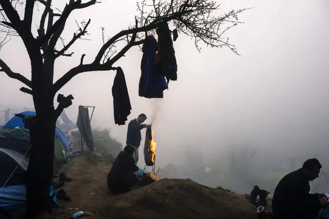 A man burns a pair of trousers to make it a bonfire during a foggy morning at a makeshift camp at the Greek-Macedonian border near the Greek village of Idomeni where thousands of refugees and migrants are stranded on March 8, 2016. European Union leaders on March 7 hailed a “breakthrough” in talks with Turkey on a deal to curb the migrant crisis but delayed a decision until a summit next week to flesh out the details of Ankara's new demands. (Photo by Dimitar Dilkoff/AFP Photo)