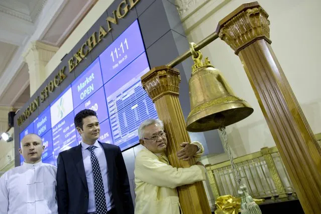 Serge Pun, right, executive chairman of First Myanmar Investment, joyfully hugs a bell pillar as electronic trading commence listing his company during the opening day of trading at Yangon Stock Exchange in Yangon, Myanmar, Friday, March 25, 2016. Myanmar’s new stock exchange, the Yangon Stock Exchange (YSX) officially opened for business on Friday more than three months after it was launched in December 2015. (Photo by Gemunu Amarasinghe/AP Photo)