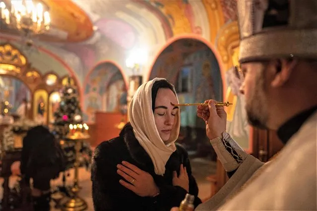 An Orthodox priest offers the holy communion to a woman during Christmas church service in Kostyantynivka, Ukraine, Friday, January 6, 2023. (Photo by Evgeniy Maloletka/AP Photo)