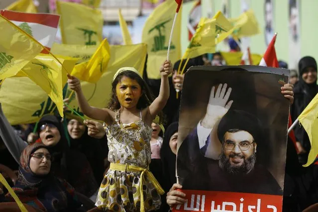 A Hezbollah supporter holds up a portrait of Hezbollah leader Sheikh Hassan Nasrallah as others wave Hezbollah and Lebanese flags during a rally commemorating “Liberation Day”, which marks the withdrawal of the Israeli army from southern Lebanon in 2000, in the southern town of Nabatiyeh, Lebanon, Sunday, May 24, 2015. (Photo by Mohammed Zaatari/AP Photo)