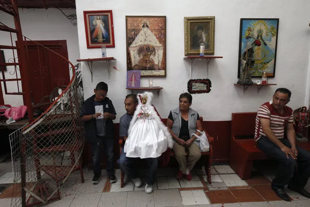 In this Feb. 19, 2017 photo, a family of devotees to the Death Saint or “Santa Muerte” hold a statue of the folk saint in a white dress at Mercy Church on the edge of Mexico City's Tepito neighborhood. The colors of the saint's vestments are associated with the type of petitions made. (Photo by Marco Ugarte/AP Photo)