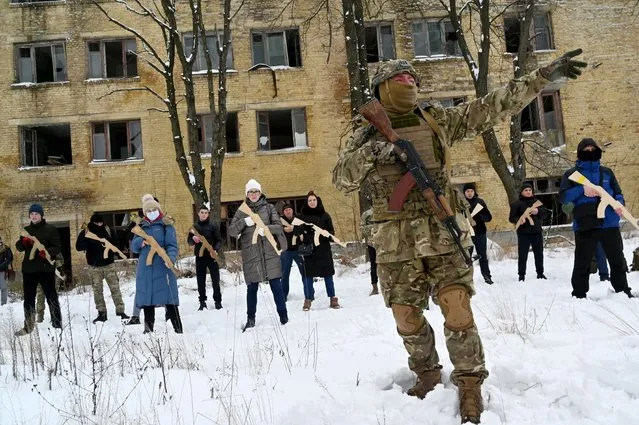 A military instructor teaches civilians holding wooden replicas of Kalashnikov rifles, during a training session at an abandoned factory in the Ukrainian capital of Kyiv on January 30, 2022. As fears grow of a potential invasion by Russian troops massed on Ukraine's border, within the framework of the training there were classes on tactics, paramedics, training on the obstacle course. The training is conducted by instructors with combat experience, members of the public initiative “Total Resistance”. (Photo by Sergei Supinsky/AFP Photo)