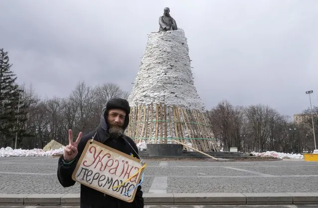 A man holds a poster reading “Ukraine will win” against the background of a monument of Taras Shevchenko, a famous Ukrainian poet and a national symbol, covered with bags to protect it from the Russian shelling in Kharkiv, Ukraine, Sunday, March 27, 2022. The bronze 16 meter high monument was opened in 1935, survived WWII and is considered one of the world's best monuments to Shevchenko. Kharkiv is Ukraine's second biggest city 30 kilometers of the Russian border. (Photo by Efrem Lukatsky/AP Photo)
