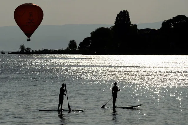 Two men steer their Stand Up Paddle boards on Lake Geneva as a hot-air balloon takes off nearby the 49th Montreux Jazz Festival, in Montreux, Switzerland, 13 July 2015. (Photo by Laurent Gillieron/EPA)