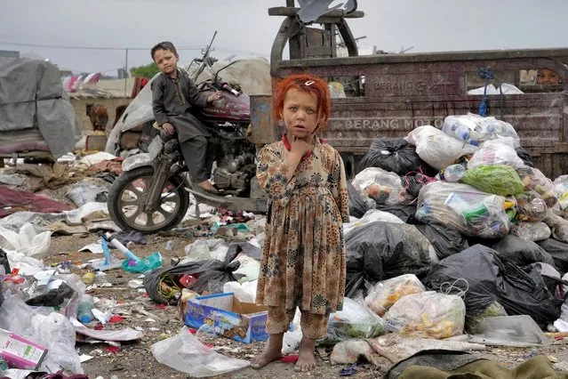 Two Afghan children  stand amid piles of garbage next to their home, in Kabul, Afghanistan, Monday, April 18, 2022. (Photo by Ebrahim Noroozi/AP Photo)