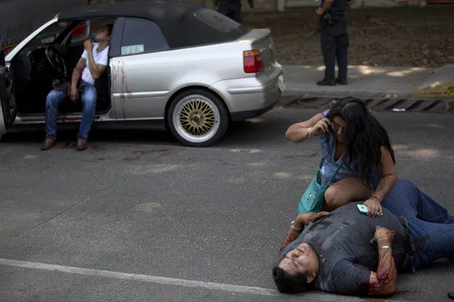In this May 13, 2016 photo, a woman talks on a phone over a wounded Edgar Osvaldo Vega, as Pedro Gracias sits in a car bleeding, waiting for assistance after being shot by unknown gunmen while driving near Caleta beach in Acapulco, Mexico. Police showed up, but when no ambulance arrived, relatives or friends simply bundled the men into private vehicles to take them to the hospital. Police marked spent shell casings with cut-off plastic soda bottles, but there was no sign of any in-depth investigation. (Photo by Enric Marti/AP Photo)