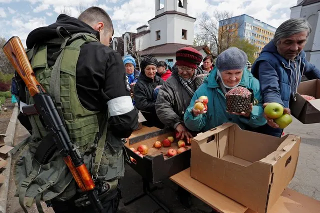 Local residents receive Easter cakes and apples handed out by service members of pro-Russian troops on Easter Day at the Svyato-Troitsky church, amid Ukraine-Russia conflict, in the southern port city of Mariupol, Ukraine on April 24, 2022. (Photo by Alexander Ermochenko/Reuters)