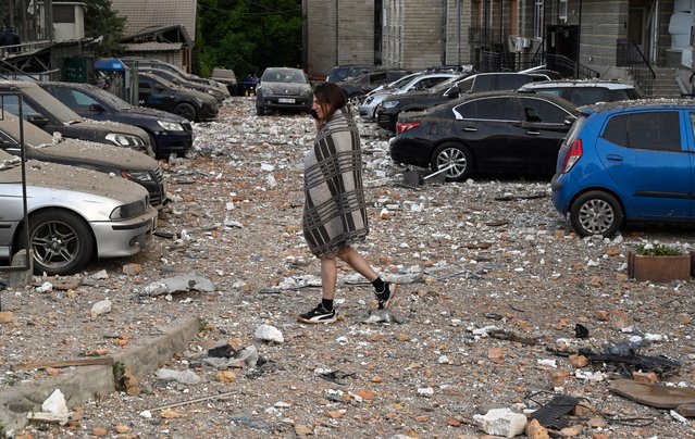 A local resident walks among damaged cars as leaving a multi-storey residential building, partially destroyed after night drone attacks in Kyiv on May 30, 2023. Ukraine on May 30, 2023 said it had downed 29 out of 31 drones, mainly over Kyiv and the Kyiv region in the latest Russian barrage – the third on the capital in 24 hours. (Photo by Sergei Supinsky/AFP Photo)