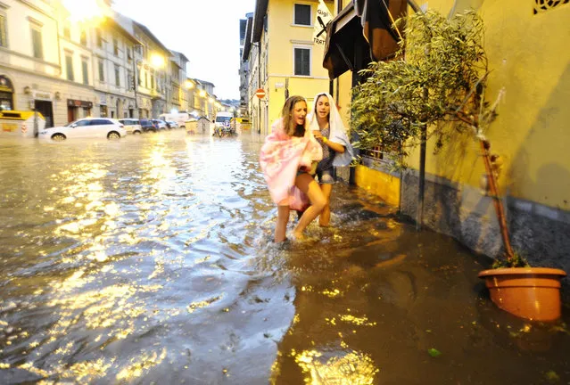 In this picture taken Saturday, August 1, 2015, people make their way on a flooded street in Florence, Italy. A thunderstorm, hail and fierce winds Saturday evening pummeled Florence, flooding basements and knocking down hundreds of trees. (Photo by Maurizio Degl'Innocenti/ANSA Via AP Photo)