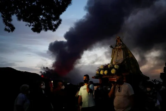 Faithful walk in a procession with the Virgen del Pino (The Pine Virgin) around its chapel to pray for the Cumbre Vieja volcano to stop as it continues to erupt in the background at El Paso, on the Canary Island of La Palma, Spain, October 19, 2021. (Photo by Susana Vera/Reuters)