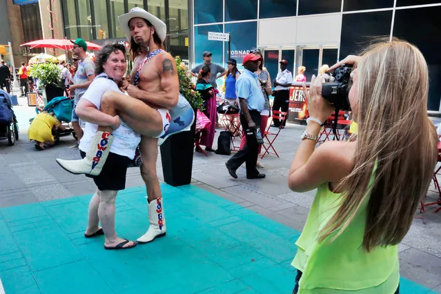 Robert Burck, The Naked Cowboy, poses for photos in one of Times Square's new color-coded designated activity zones, Tuesday, June 21, 2016, in New York. Street performers and costumed characters can be issued summonses or face arrest if they're caught operating outside the eight designated rectangles, under new rules aimed at controlling overly aggressive street performers. Each area is painted teal and measures 8 feet by 50 feet. (Photo by Richard Drew/AP Photo)