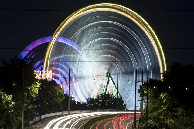 The July 17, 2017 long-time exposed photo shows cars passing by ferris wheels at a fun fair in Duesseldorf, western Germany. (Photo by Federico Gambarini/DPA via AP Photo)