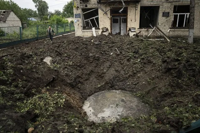 A local man walks in front of a crater and damaged school after Russian shelling at residential area in Chuhuiv, Kharkiv region, Ukraine, Saturday, July 16, 2022. (Photo by Evgeniy Maloletka/AP Photo)