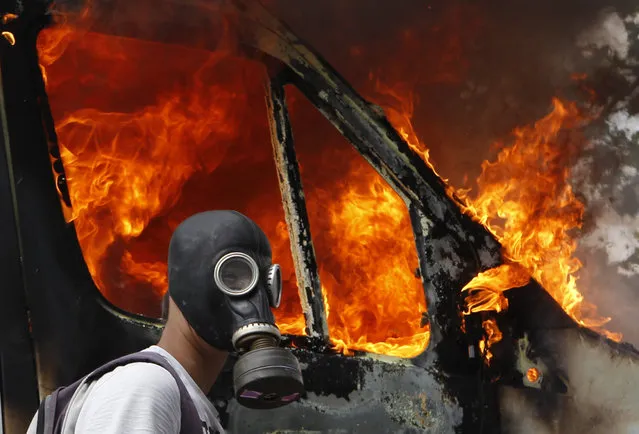 A protester wearing a gas mask walks beside a burning van during violent protests against austerity measures in Athens, June 28, 2011. (Photo by Yannis Behrakis/Reuters)