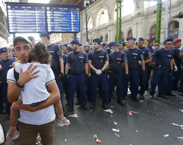 A migrant carries his child in front of a line of hungarian policemen at the main Eastern Railway station in Budapest, Hungary, September 1, 2015. (Photo by Laszlo Balogh/Reuters)