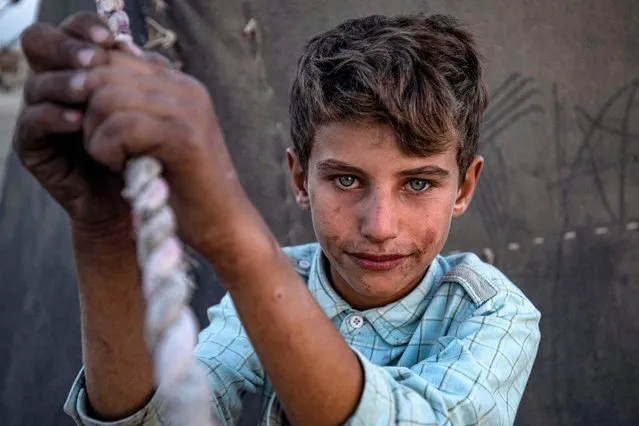 A boy looks on as he holds the rope of a tent at the “Yunani” (Greek) camp for Syrians displaced by conflict originally from the countryside of Raqa and Hamah and other regions, along the banks of the Euphrates river in Syria's northern province of Raqa on October 13, 2022. (Photo by Delil Souleiman/AFP Photo)