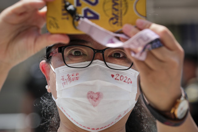 A woman wearing a face mask to protect against the new coronavirus films students leave the school after finishing the first day of China's national college entrance examinations, known as the gaokao, in Beijing, Tuesday, July 7, 2020. China's college entrance exams began in Beijing on Tuesday after being delayed by a month due to the coronavirus outbreak. (Photo by Andy Wong/AP Photo)