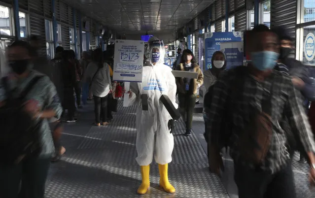 An employee wearing protective gear as a precaution against the new coronavirus holds banner displaying information about the virus and those infected at the Harmoni Central Busway station in Jakarta Thursday, July 16, 2020. Indonesia has the highest numbers of coronavirus infections and fatalities in Southeast Asia. (Photo by Achmad Ibrahim/AP Photo)