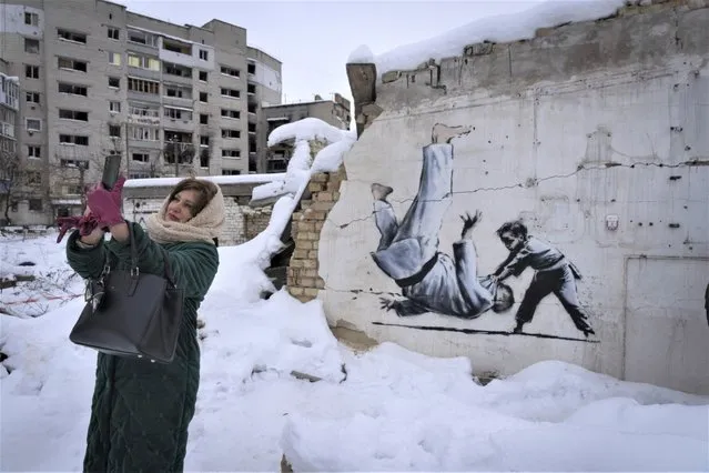 A woman takes a selfie at an artwork that was made by British street artist Banksy on a building destroyed by the Russian army in Borodyanka, Kyiv region, Ukraine, Tuesday, December 6, 2022. (Photo by Efrem Lukatsky/AP Photo)