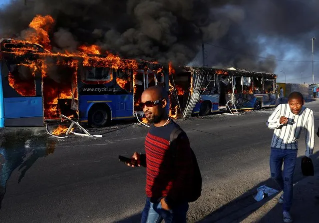 People walk past a torched bus during a two-day strike by taxi operators over a number of grievances against traffic authorities in Cape Town, South Africa on November 21, 2022. (Photo by Esa Alexander/Reuters)