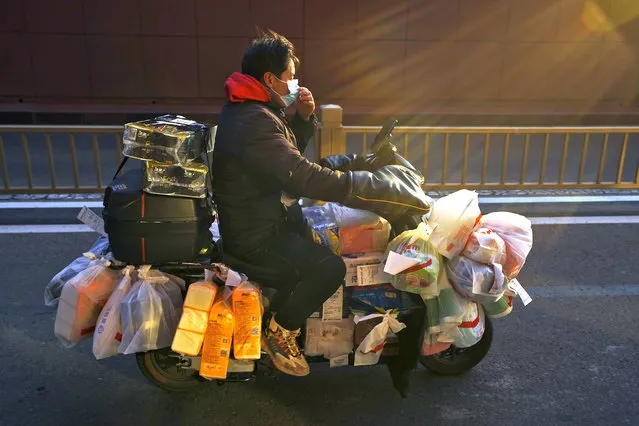 A delivery worker adjusts his face mask as he rides on his bike loaded with customers' online order groceries on a street in Beijing, Wednesday, January 4, 2023. As the virus continues to rip through China, global organizations and governments have called on the country to start sharing data while others have criticized its current numbers as meaningless. Throughout the pandemic, the country's dearth of information has prompted caution and weariness. (Photo by Andy Wong/AP Photo)