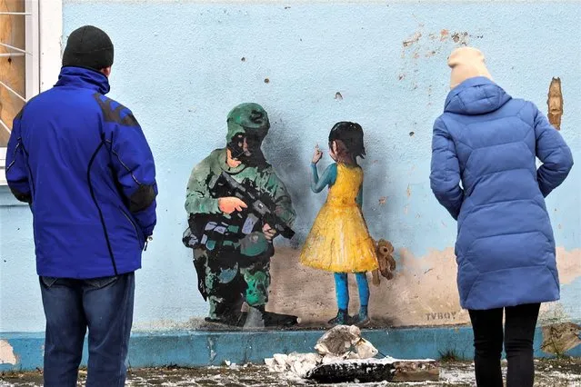 People look at an artwork of the famous street artist Tvboy, created on a wall of the House of Culture, which was heavily damaged during Russia's attack on Ukraine, in the town of Irpin, outside Kyiv, Ukraine on January 29, 2023. (Photo by Valentyn Ogirenko/Reuters)