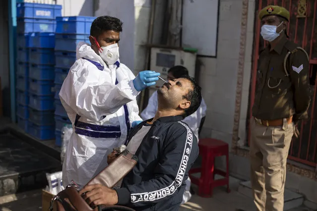 A health worker takes a nasal swab sample to test for COVID-19 during random testing of people infront of a shop at Delhi-Noida border on the outskirts of New Delhi, India, Saturday, November 21, 2020. (Photo by Altaf Qadri/AP Photo)