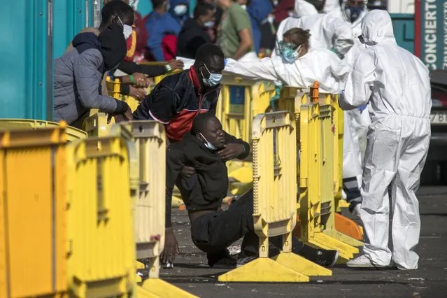 An African migrant is helped off the floor at Arguineguin port after their rescue in Gran Canaria island, Spain on Wednesday November 25, 2020. Spanish rescue services said Wednesday at least seven people died after a migrant boat carrying more than 30 people hit rocks close to a small port on the Canary Island of Lanzarote. Many of the rescued were taken to the Arguineguín dock on the southwestern coast of Gran Canaria island, where several thousand people of different origin are being kept, some in tents. (Photo by Javier Fergo/AP Photo)