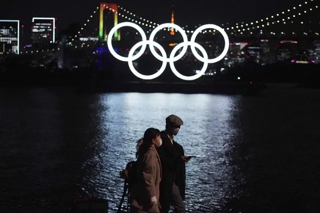 A man and a woman walk past near the Olympic rings floating in the water in the Odaiba section Tuesday, December 1, 2020, in Tokyo. The Olympic Symbol was reinstalled after it was taken down for maintenance ahead of the postponed Tokyo 2020 Olympics. (Photo by Eugene Hoshiko/AP Photo)