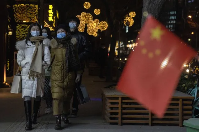 Patrons wearing masks to protect from the coronavirus past by a Chinese national flag as they visit a bar street on New Year Eve in Beijing on Thursday, December 31, 2020. This New Year's Eve is being celebrated like no other, with pandemic restrictions limiting crowds and many people bidding farewell to a year they'd prefer to forget. (Photo by Ng Han Guan/AP Photo)