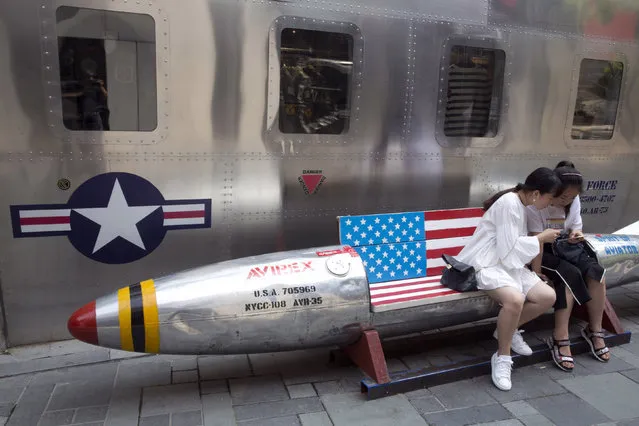 Chinese women look at phone near a rocket shaped bench with an American flag used as a marketing gimmick for a U.S. apparel shop in Beijing, China, Friday, July 6, 2018. The United States hiked tariffs on Chinese imports Friday and Beijing said it immediately retaliated in a dispute between the world's two biggest economies that President Donald Trump says he is prepared to escalate. (Photo by Ng Han Guan/AP Photo)