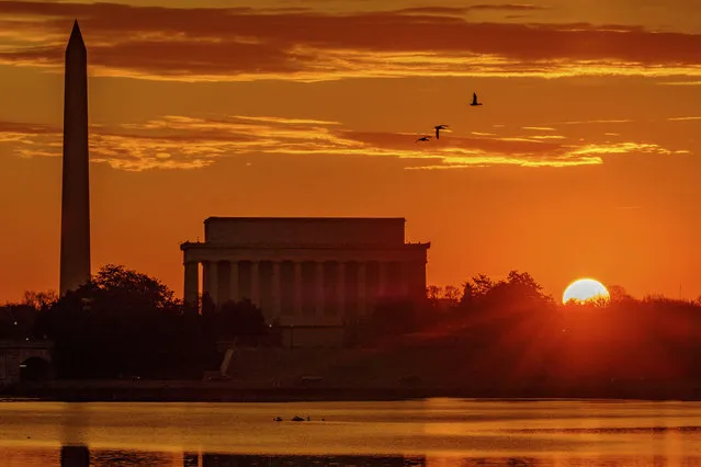 The sun peaks over the horizon next to the Washington Monument and Lincoln Memorial at daybreak along the Potomac River in Washington, Tuesday, March 6, 2018. (Photo by J. David Ake/AP Photo)