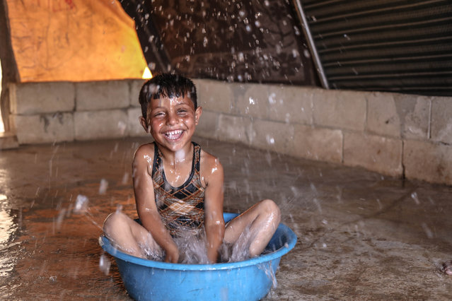 A child sitting in a washbowl filled with water cools himself as civilians struggle with protecting themselves from the dangers of extreme heat at the refugee camp, in Idlib, Syria on July 13, 2023. The civilians, who fled from the attacks of the Syrian Army, live under harsh conditions without infrastructure and electricity while the temperature reaches 47 Celsius in the region. (Photo by Izzeddin Kasim/Anadolu Agency via Getty Images)