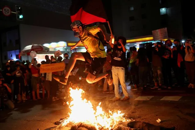 A man jumps over a burning doll depicting Brazilian President Jair Bolsonaro during a protest against him, in front of the Museum of Modern Art in Sao Paulo, Brazil, May 29, 2021. (Photo by Amanda Perobelli/Reuters)