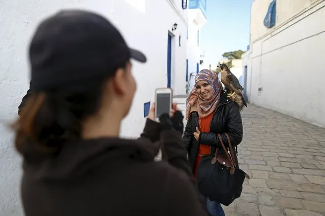 Falconer Maroua (L), for the price of a few dinars, photographs a woman as she poses with a falcon on her shoulder in Sidi Bou Said, a popular tourist destination near Tunis, Tunisia, February 2, 2016. Meroua says she uses her falcon to liven up the area for tourists as a business. “I am disappointed by the 2011 revolution. It brought nothing good. Since the last terrorists attacks, visits by foreign tourists are becoming increasingly rare. In fact, we are dealing only with local tourists. (Photo by Zohra Bensemra/Reuters)