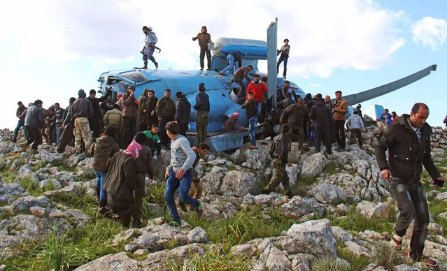 People gather around a helicopter reportedly belonging to the Syrian regime forces that crashed on March 22, 2015 in Jabal al-Zawiya in the northwest province of Idlib. Islamist rebels captured four crew members when the helicopter crashed, while a fifth serviceman was killed. (Photo by Ghaith Omran/AFP Photo)