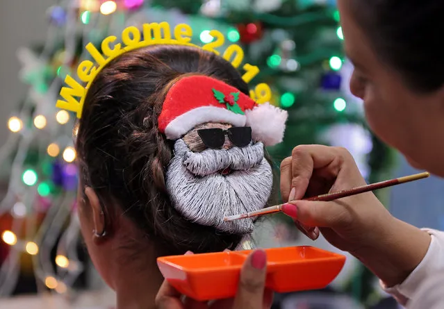 A make-up artist decorates the hair of a woman in the shape of Santa Claus during the New Year preparations in Ahmedabad, India, December 31, 2018. (Photo by Amit Dave/Reuters)