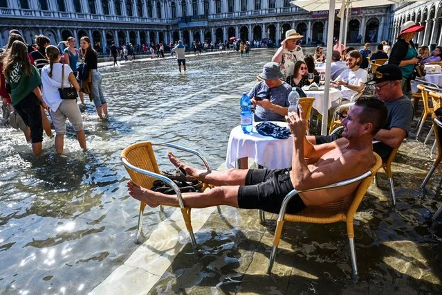 Tourists sit at a cafe's terrace on a flooded St. Mark's square in Venice on September 27, 2022, following an “Alta Acqua” high tide event, too low to operate the MOSE Experimental Electromechanical Module that protects the city of Venice from floods, but high enough to potentially threaten St. Mark's Basilica. (Photo by Andrea Pattaro/AFP Photo)