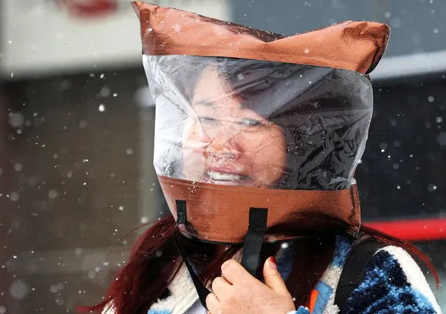 A woman uses a plastic bad to protect her head amid snowfall in Beijing, China on December 14, 2023. (Photo by Tingshu Wang/Reuters)