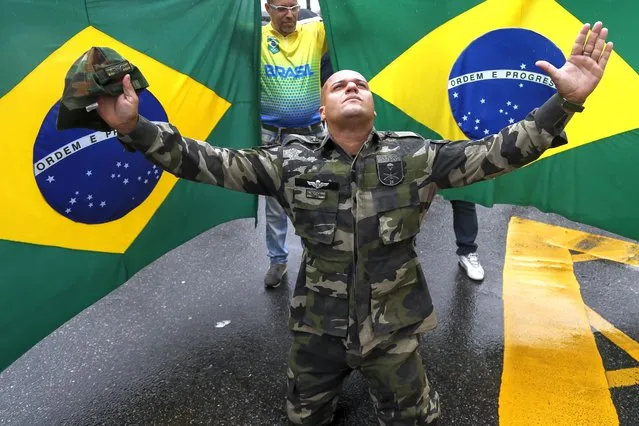 A supporter of President Jair Bolsonaro dressed in fatigues, kneels with his arms spread out in front of Brazilian national flags, during a protest against Bolsonaro's defeat in the presidential runoff election, in Rio de Janeiro, Brazil, Wednesday, November 2, 2022. Thousands of supporters called on the military Wednesday to keep the far-right leader in power, even as his administration signaled a willingness to hand over the reins to his rival Luiz Inacio Lula da Silva. (Photo by Bruna Prado/AP Photo)