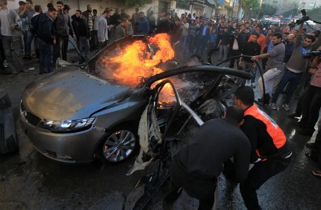 Palestinians extinguish fire from the car of Ahmed Jaabari,  head of the military wing of the Hamas movement, the Ezzedin Qassam Brigades, after it was hit by an Israeli air strike in Gaza City on November 14, 2012. (Photo by Mahmud Hams/AFP Photo)