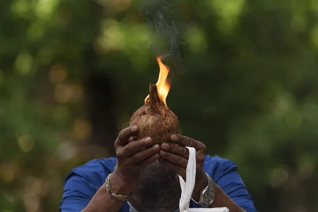 A Indian man prays with lit coconut as an offering outside a temple during the Hindu festival of lights, Diwali, in Kuala Lumpur, Malaysia, Thursday, November 4, 2021.  Millions of people across Asia are celebrating the Hindu festival of Diwali, which symbolizes new beginnings and the triumph of good over evil and light over darkness. Millions of people across Asia are celebrating the Hindu festival of Diwali, which symbolizes new beginnings and the triumph of good over evil and light over darkness. The festival is celebrated mainly in India but Hindus across the world, particularly in other parts of Asia, also gather with family members and friends to socialize, visit temples and decorate houses with small oil lamps made from clay. (Photo by Vincent Thian/AP Photo)
