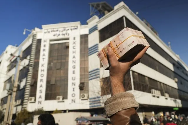 An Afghan money changer holds a stack of Iranian currency at Khorasan market in Herat, Afghanistan, Wednesday, December 15, 2021. The value of Afghanistan's currency is tumbling, exacerbating an already severe economic crisis and deepening poverty in a country where more than half the population already doesn't have enough to eat. (Photo by Mstyslav Chernov/AP Photo)