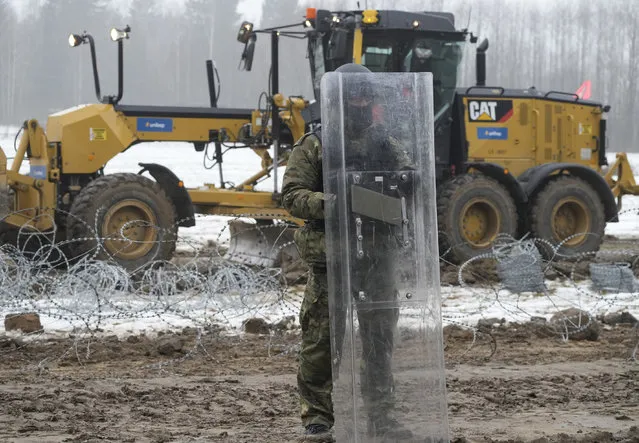 Military watching the start of work on the first part of some 180 kilometers (115 miles) of a 5.5 meter (18ft)-high metal wall intended to block migrants pushed by Belarus, in what the European Union calls a “hybrid attack”, from crossing illegally into EU territory, in Tolcze, near Kuznica, Poland, on the Polish side of the border with Belarus on, Thursday, January 27, 2022. (Photo by Czarek Sokolowski/AP Photo)