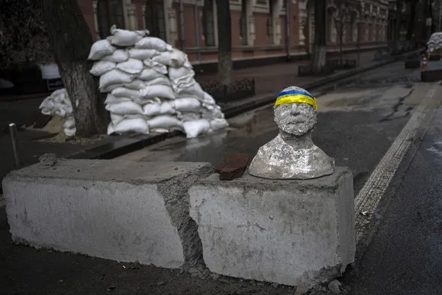 A sculpture adorned with a headband designed with the colors of the Ukraine national flag sits on top of a concrete block at a checkpoint in Kyiv, Ukraine, Saturday, March 26, 2022. With the invasion now in its second month, Russian forces have seemingly stalled on many fronts and are even losing previously taken ground to Ukrainian counterattacks, including around Kyiv. (Photo by Rodrigo Abd/AP Photo)