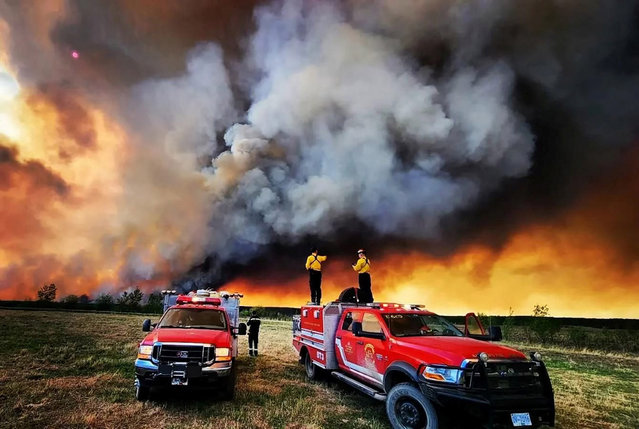 Firefighters stand on a Kamloops Fire Rescue truck at a wildfire near Fort St. John, British Columbia, Canada on May 14, 2023. (Photo by Kamloops Fire Rescue/Handout via Reuters)