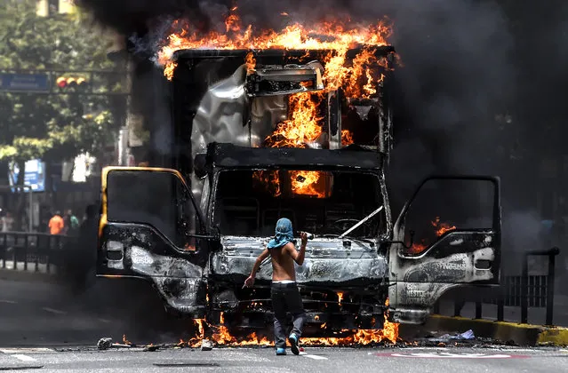 A truck set ablaze by opposition activists blocking an avenue during a protest burns in Caracas, on July 18, 2017. The Venezuelan opposition called for a 24-hour national civic strike next Thursday to pressure President Nicolas Maduro to withdraw the call to a National Constituent Assembly, after achieving a massive vote of rejection in a symbolic plebiscite. (Photo by Juan Barreto/AFP Photo)